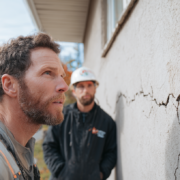 Professional foundation contractor inspecting crack in exterior concrete foundation wall with homeowner in Rhode Island, and explaining to him how to fix foundation cracks.