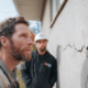 Professional foundation contractor inspecting crack in exterior concrete foundation wall with homeowner in Rhode Island, and explaining to him how to fix foundation cracks.