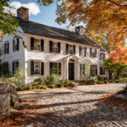 Historic Rhode Island colonial home with white clapboard siding and black shutters in fall setting, struggling with foundation issues