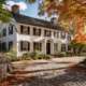 Historic Rhode Island colonial home with white clapboard siding and black shutters in fall setting, struggling with foundation issues