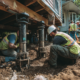 Professional repair crew installing hydraulic support systems under residential home as part of foundation lifting work