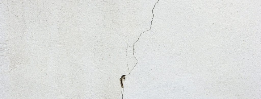 Vertical foundation crack on white painted basement wall showing typical hairline crack pattern